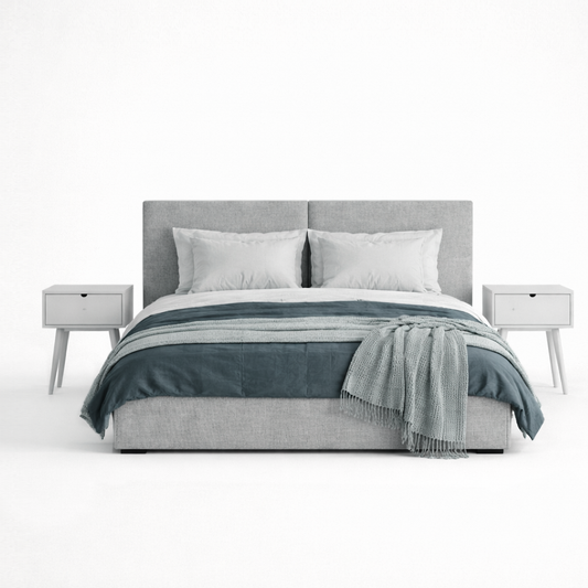 Gray upholstered bed with white bedding and a blue throw blanket on a white background