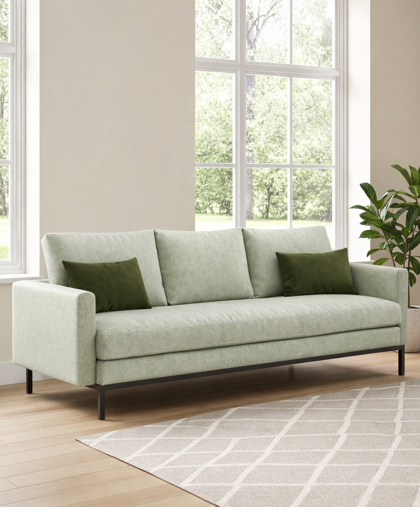 Light green sofa with green cushions in a room with large windows and a plant.