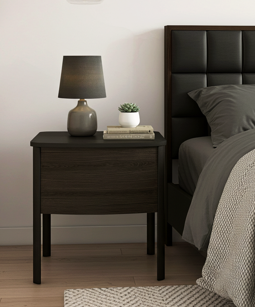 Dark wood nightstand with lamp and decor next to a bed with black upholstered headboard.