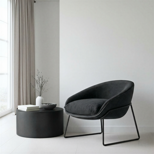 Modern black chair and round table in a minimalistic room with white walls and light grey curtains.