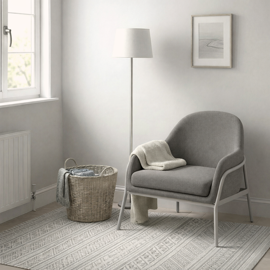 Grey armchair in a room with a lamp, basket, and window.
