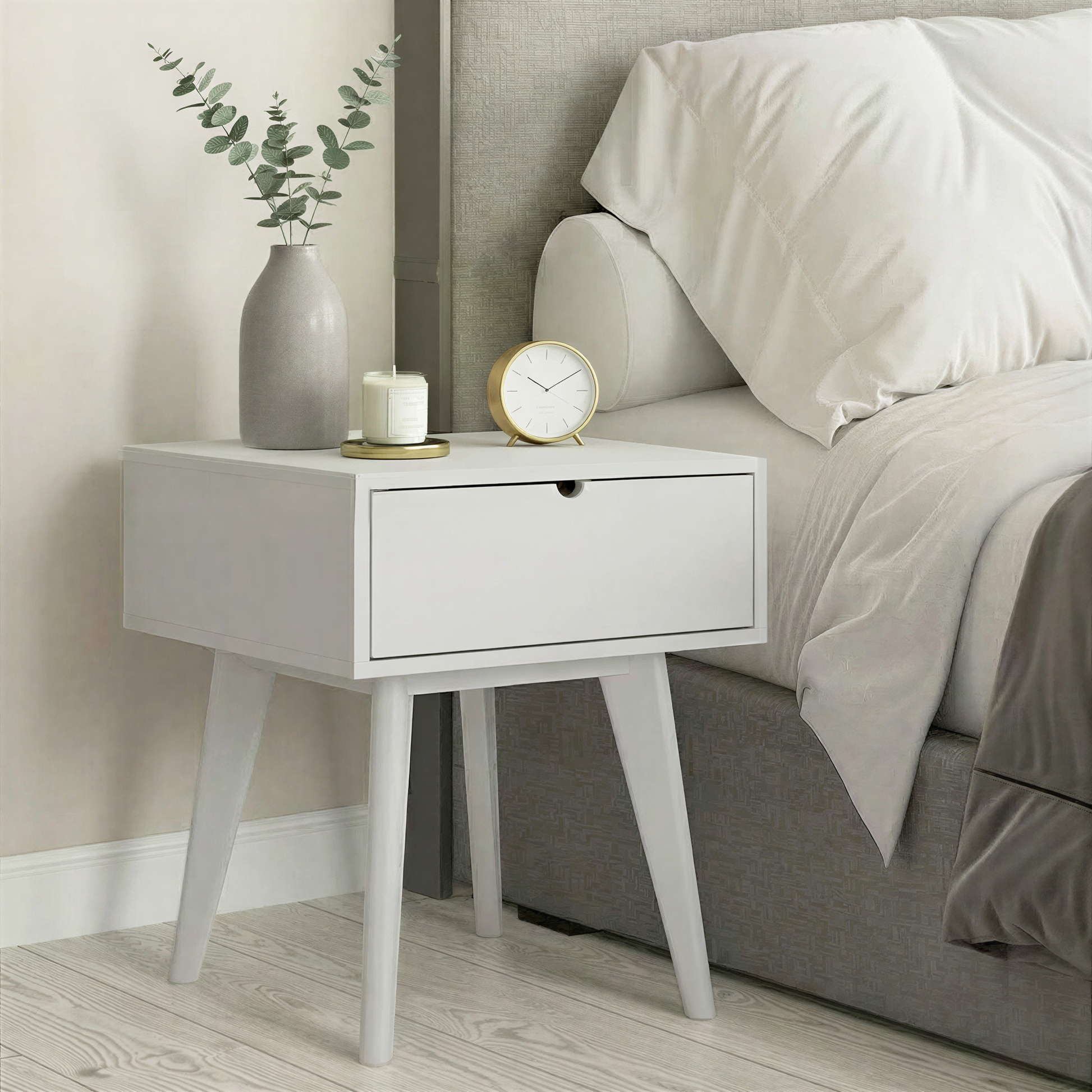 Light grey nightstand with a clock and vase next to a bed with gray bedding.