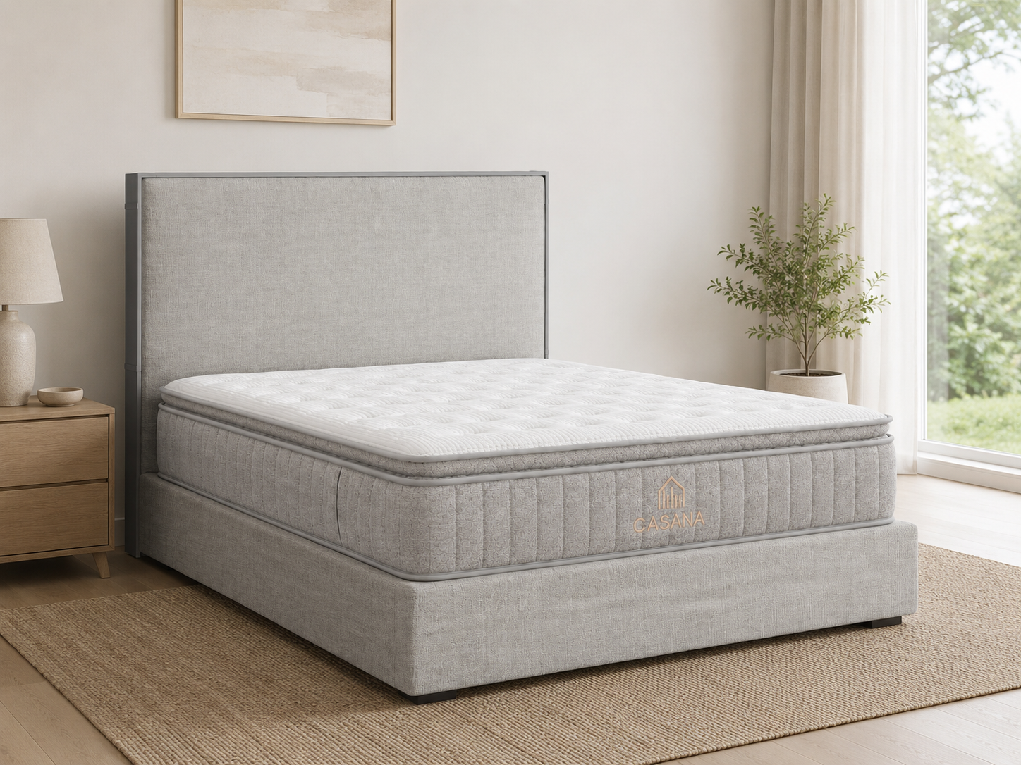 A light gray upholstered bed frame with a matching headboard and mattress, shown in a bright bedroom setting with a window, plant, and bedside table.
