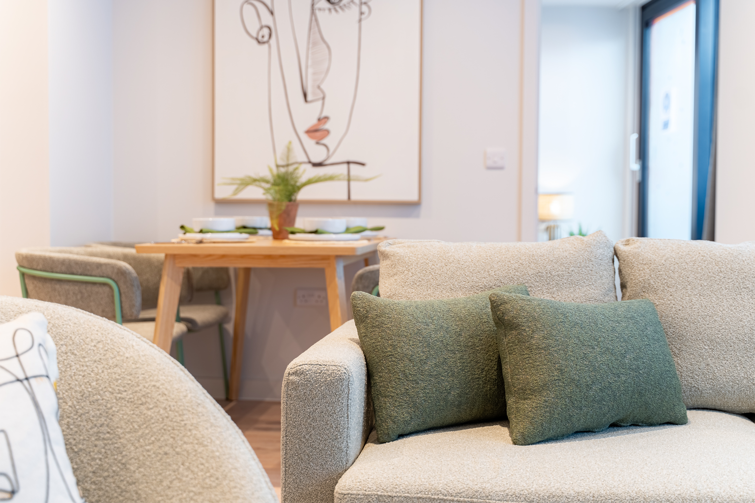 Living room with beige sofa, green cushions, and a small table with a plant.
