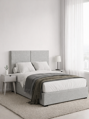 Grey upholstered bed in a minimalistic bedroom with white walls and a rug.